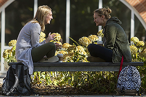 Two students sitting a bench facing each other